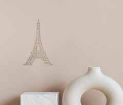 Decorative Eiffel Tower wall art on a beige wall with a white vase and box below.