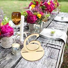 Decorative gold card holder on a table with floral arrangements and glasses outdoors.