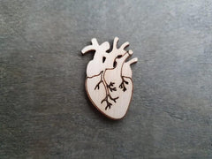 Wooden anatomical heart pin on a dark surface