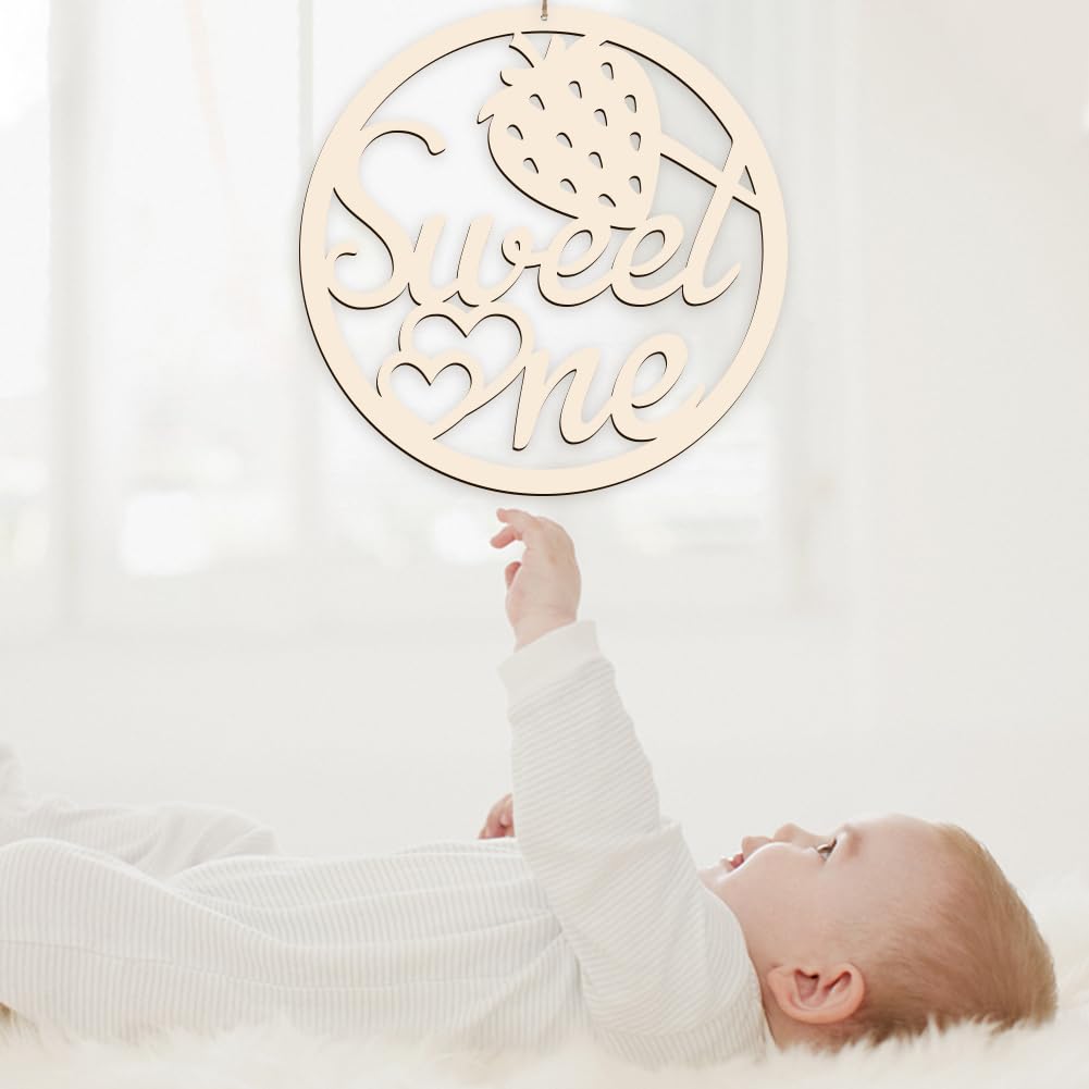 Baby reaching towards a decorative wooden sign with 'Sweet One' text on a white background