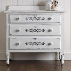 White dresser with decorative carvings on a wooden floor.
