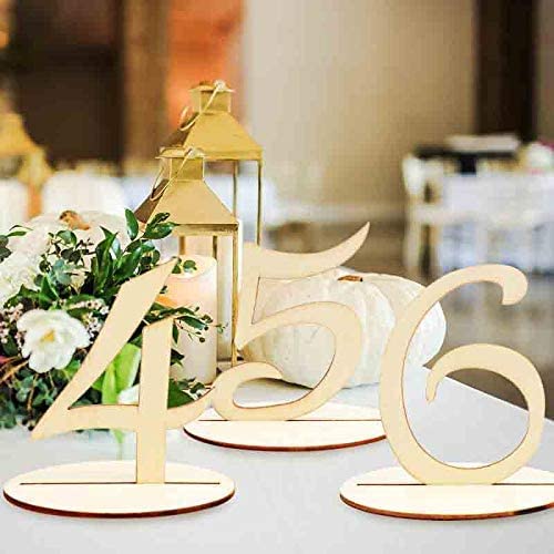 Wooden table numbers on a table with a candle lantern and flowers in the background