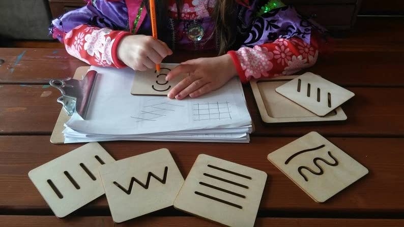 Child writing with a pencil on paper, surrounded by educational materials on a wooden table.
