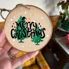 Wooden ornament with 'Merry Christmas' text and trees held by a hand.