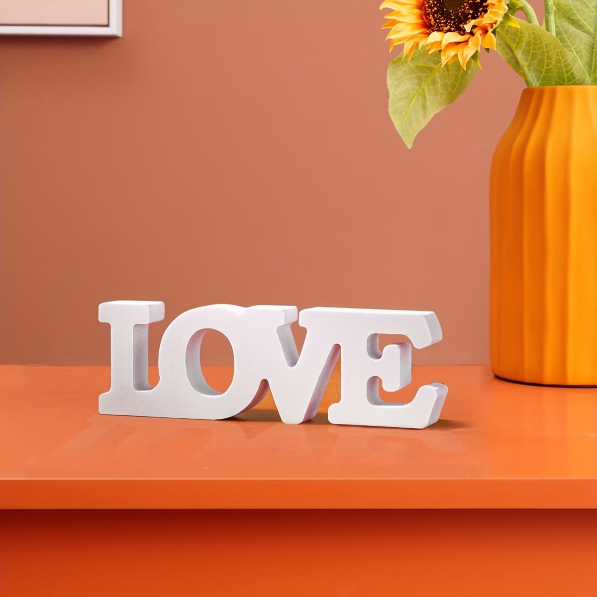 White 'LOVE' letters on an orange surface with a sunflower in the background