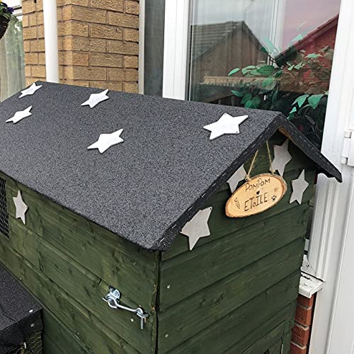 Green wooden shed with gray roof and decorative stars, set against a brick wall and glass door.