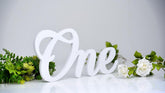 White decorative letter 'One' with greenery on a light gray background