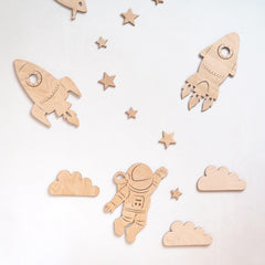 Wooden space-themed cutouts including rockets, stars, clouds, and an astronaut on a light gray background.