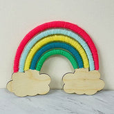 Colorful yarn rainbow with wooden cloud shapes on a light background