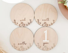 Four wooden discs with milestone markings for a baby's growth, including 'week', 'month', and '1 year'.