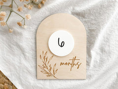 Wooden baby milestone card with '6 months' on a white fabric background