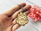 Wooden owl keychain held in a hand with pink flowers in the background