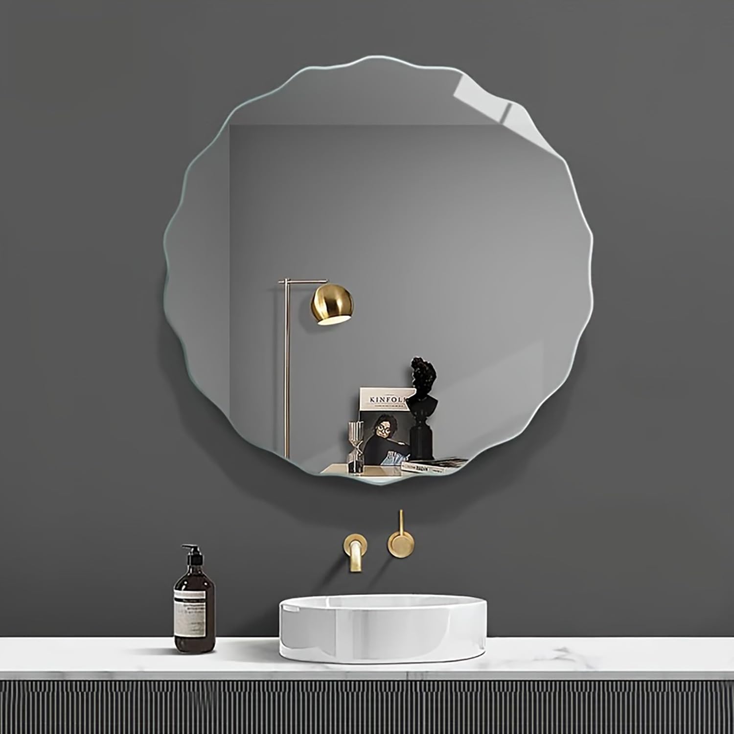 Round mirror on a gray wall above a sink with decorative items.
