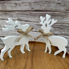Two white deer figurines with burlap bows on a wooden surface and background.