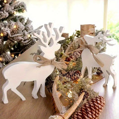 White deer figurines with burlap ribbons on a Christmas-themed table setting with pinecones and greenery.