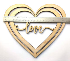 Wooden heart-shaped cutout with 'love' text and a ruler for scale on a white background