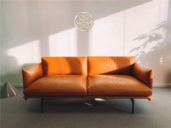 Brown leather sofa in a room with a light gray wall and a decorative ceiling light fixture.