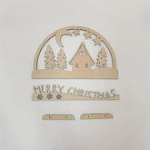 Wooden Christmas decoration with house, trees, and 'Merry Christmas' text on a white background