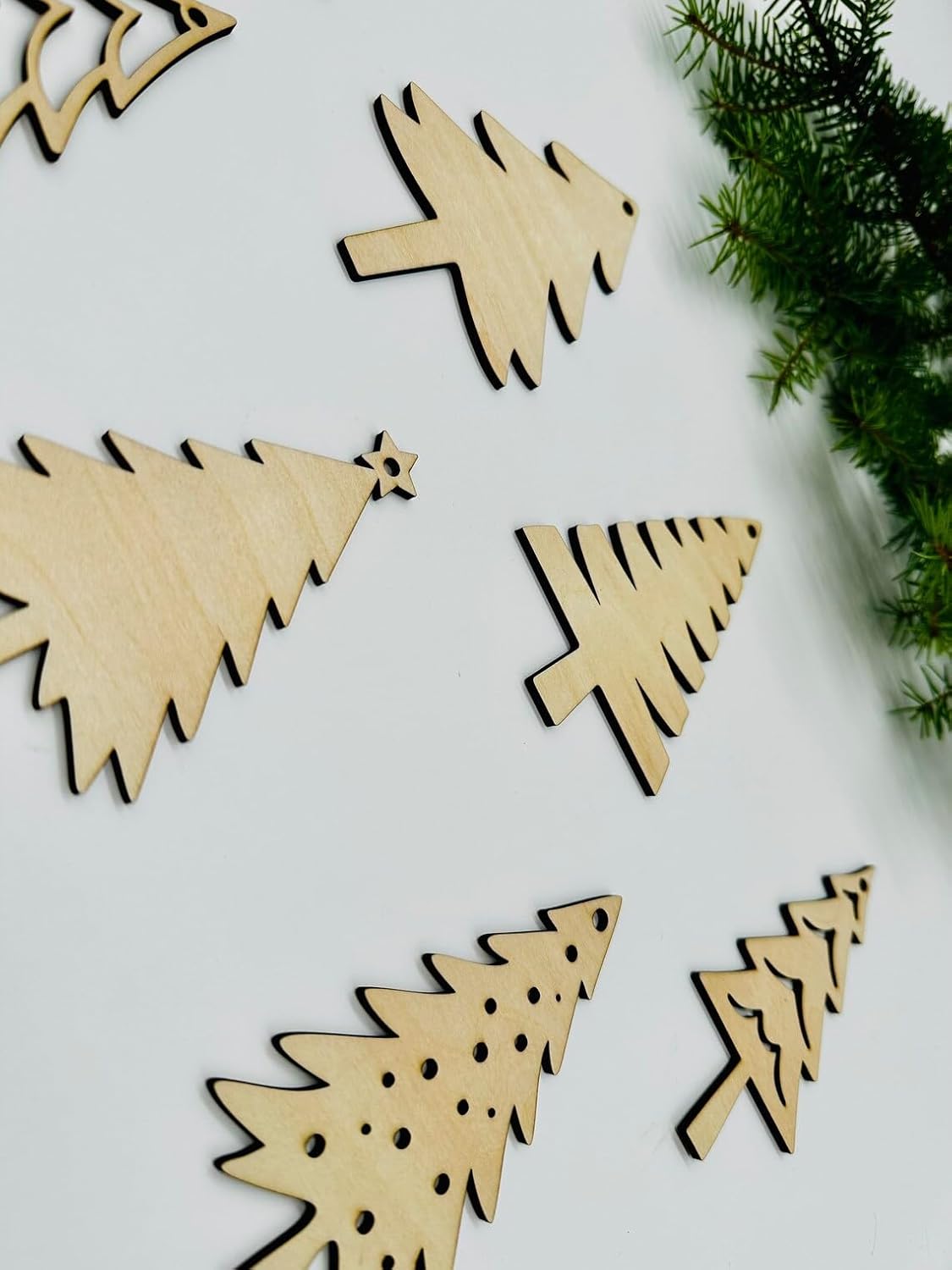 Wooden Christmas tree ornaments on a white surface with greenery.