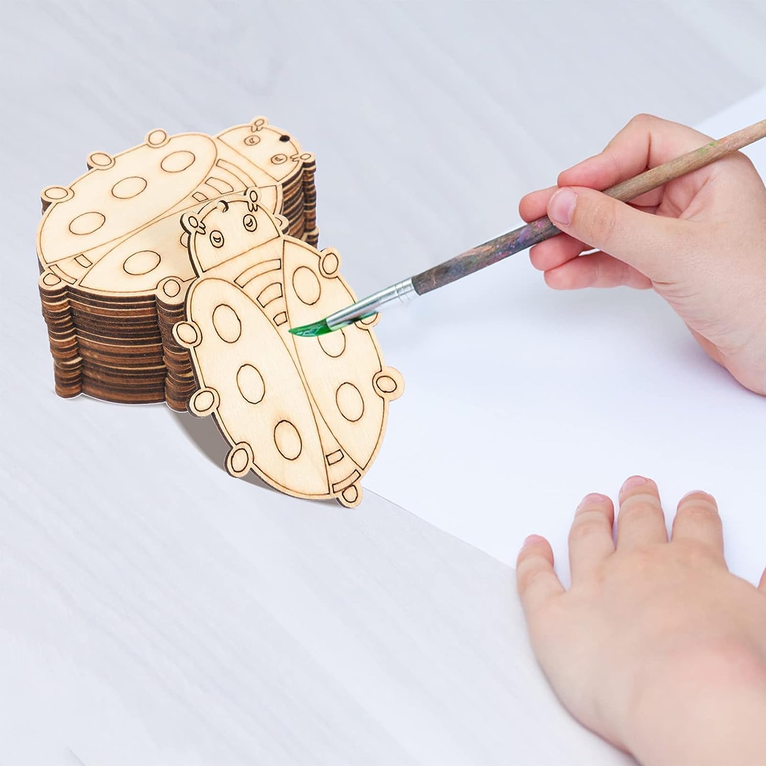 Wooden ladybug shapes with a hand painting one of them on a white surface.