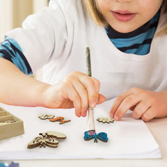 Child painting wooden butterfly figurines with a paintbrush on a white surface.