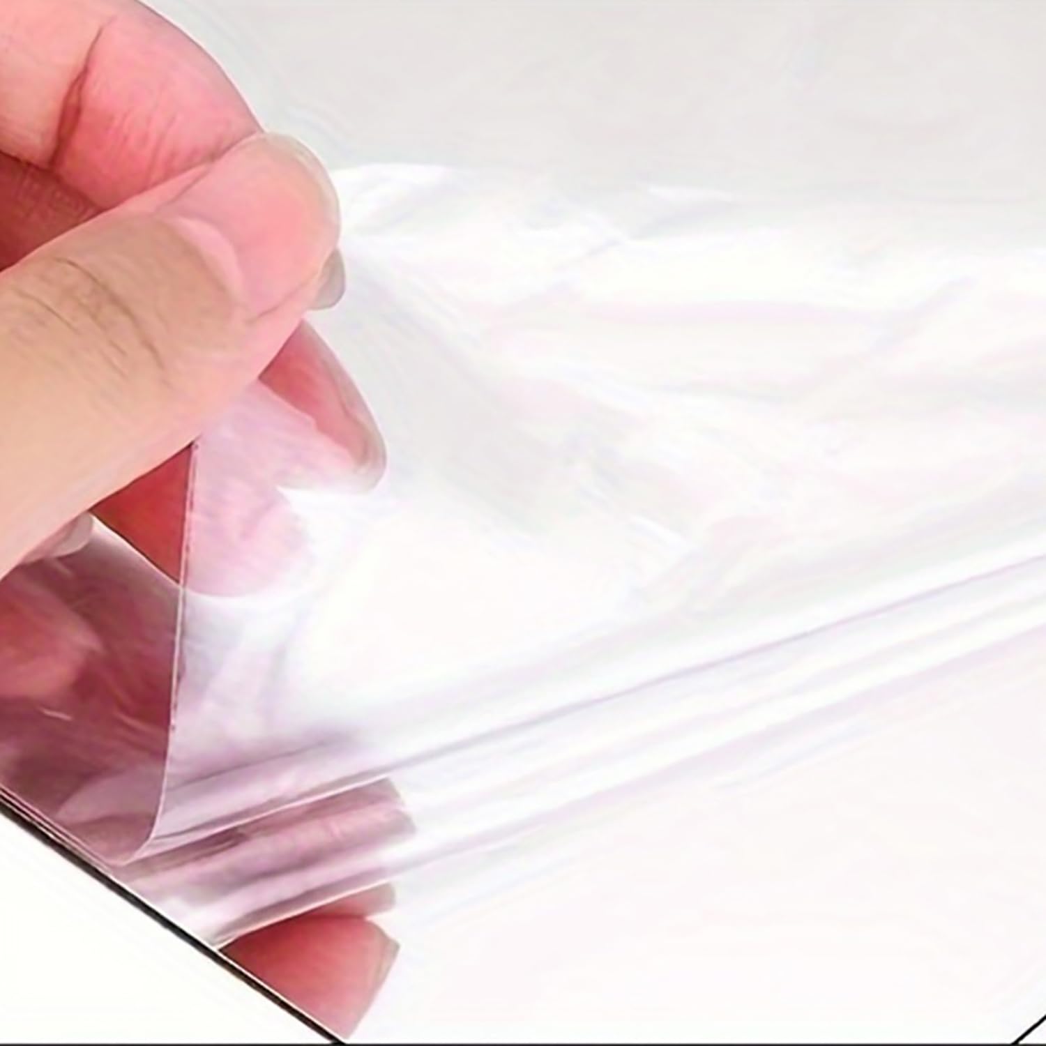 Hand holding a clear plastic sheet against a white background