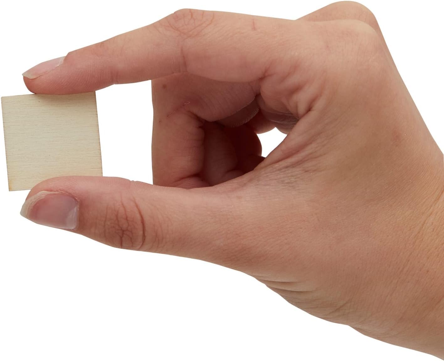 Hand holding a small square piece of wood against a white background