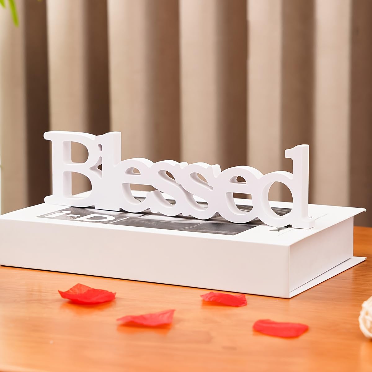 Decorative word 'Blessed' on a book with red flower petals on a wooden surface.