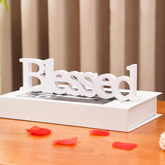 Decorative word 'Blessed' on a book with red flower petals on a wooden surface.