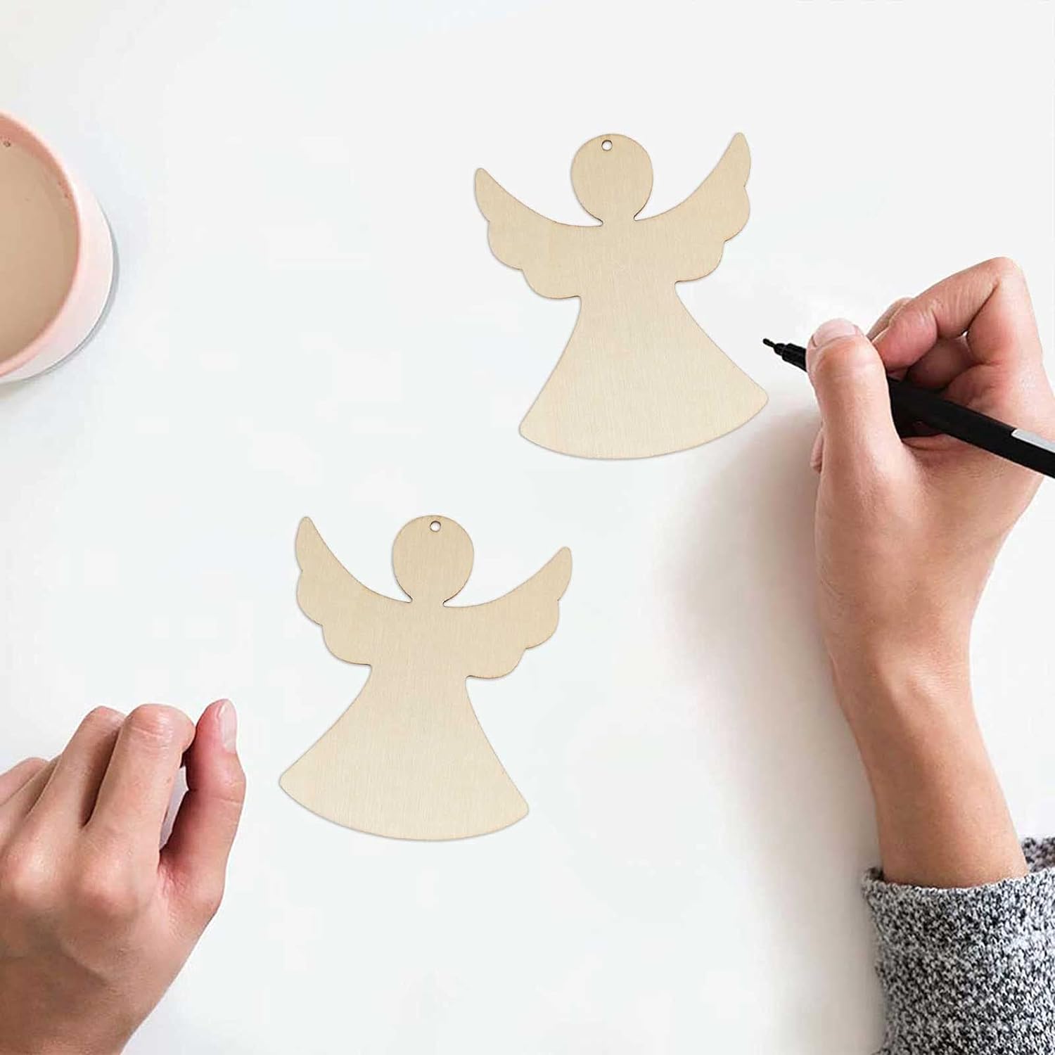 Wooden angel shapes with hands using a marker on a white background