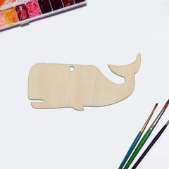 Wooden whale-shaped craft on a white surface with watercolor paints and brushes.