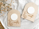 Two wooden baby milestone cards with floral designs and 'months' text on a white fabric background.