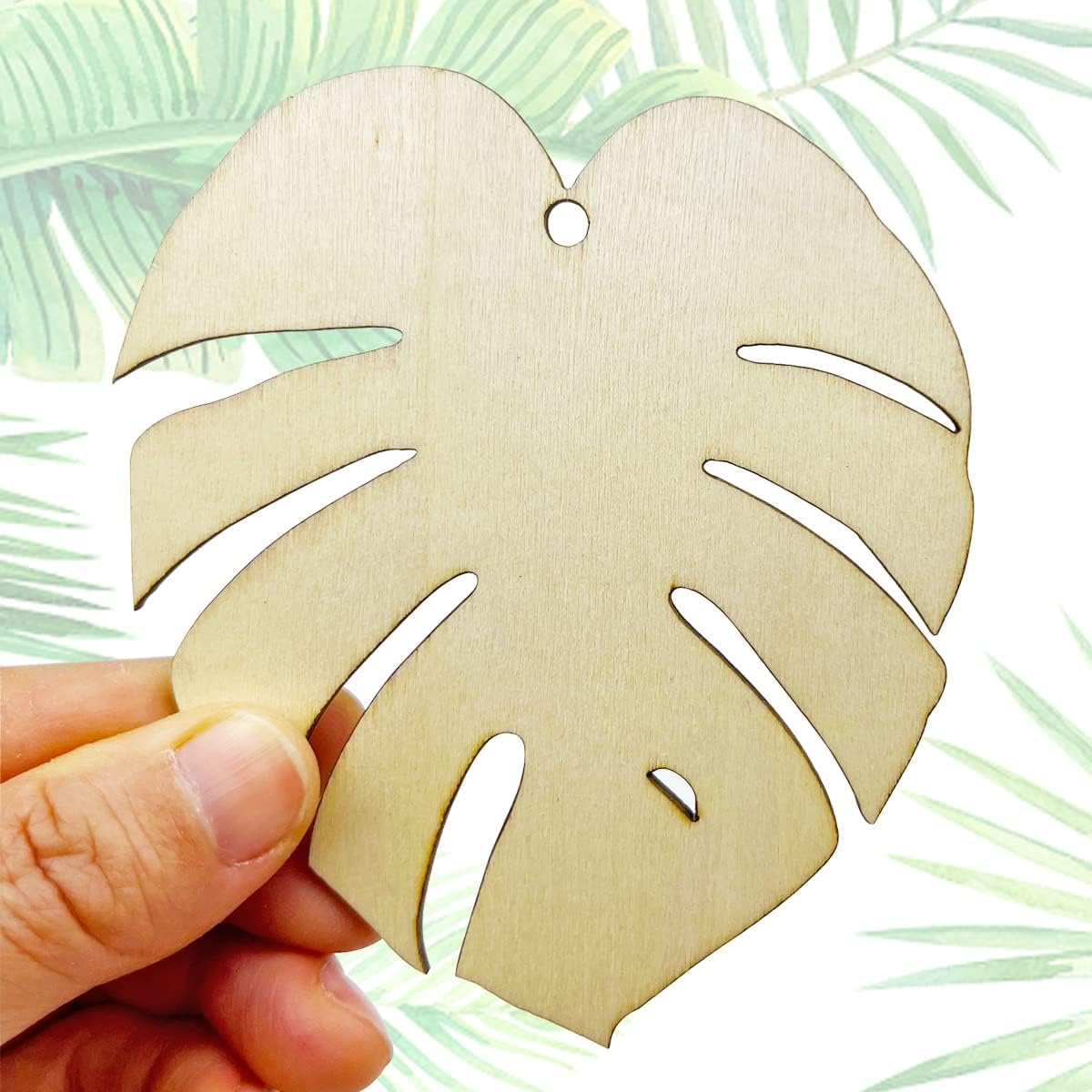 Wooden leaf-shaped ornament held by a hand with a tropical leaf pattern in the background