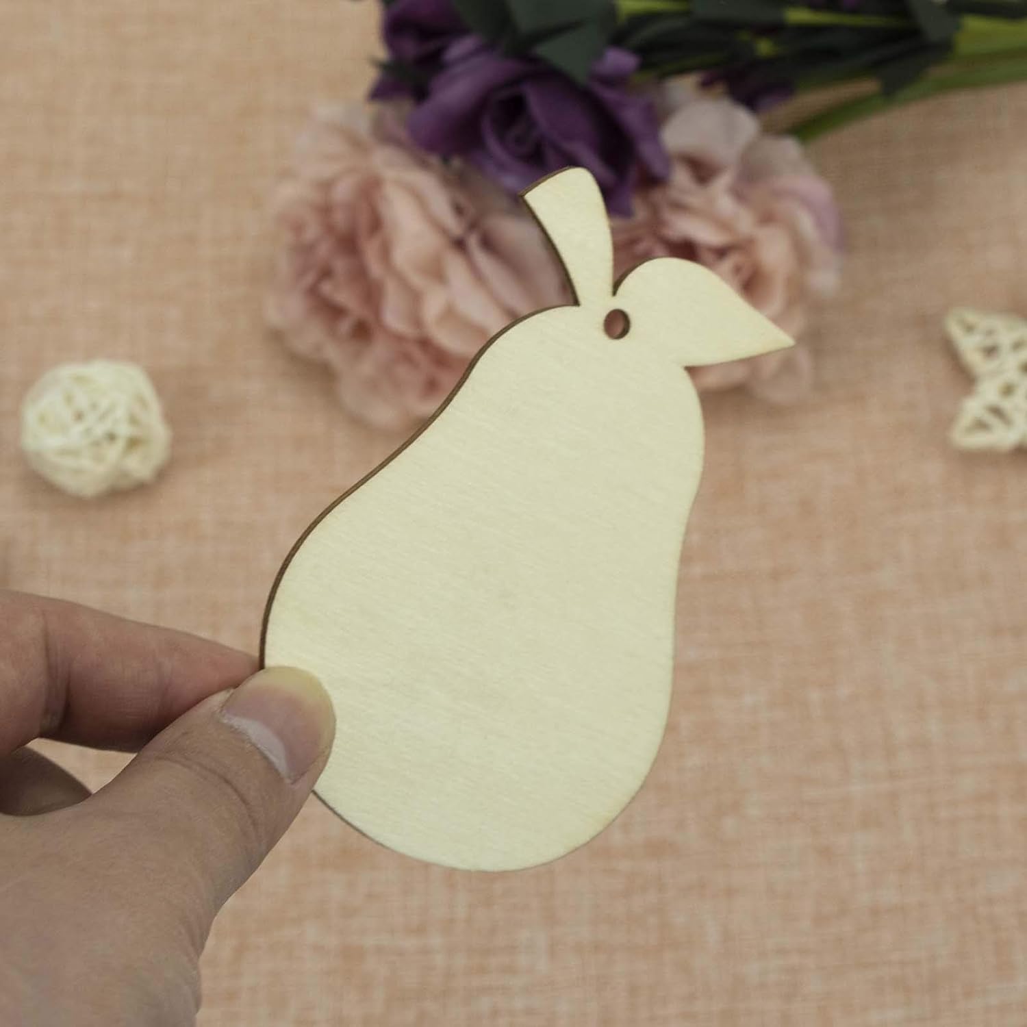 Hand holding a wooden bird-shaped tag with flowers in the background