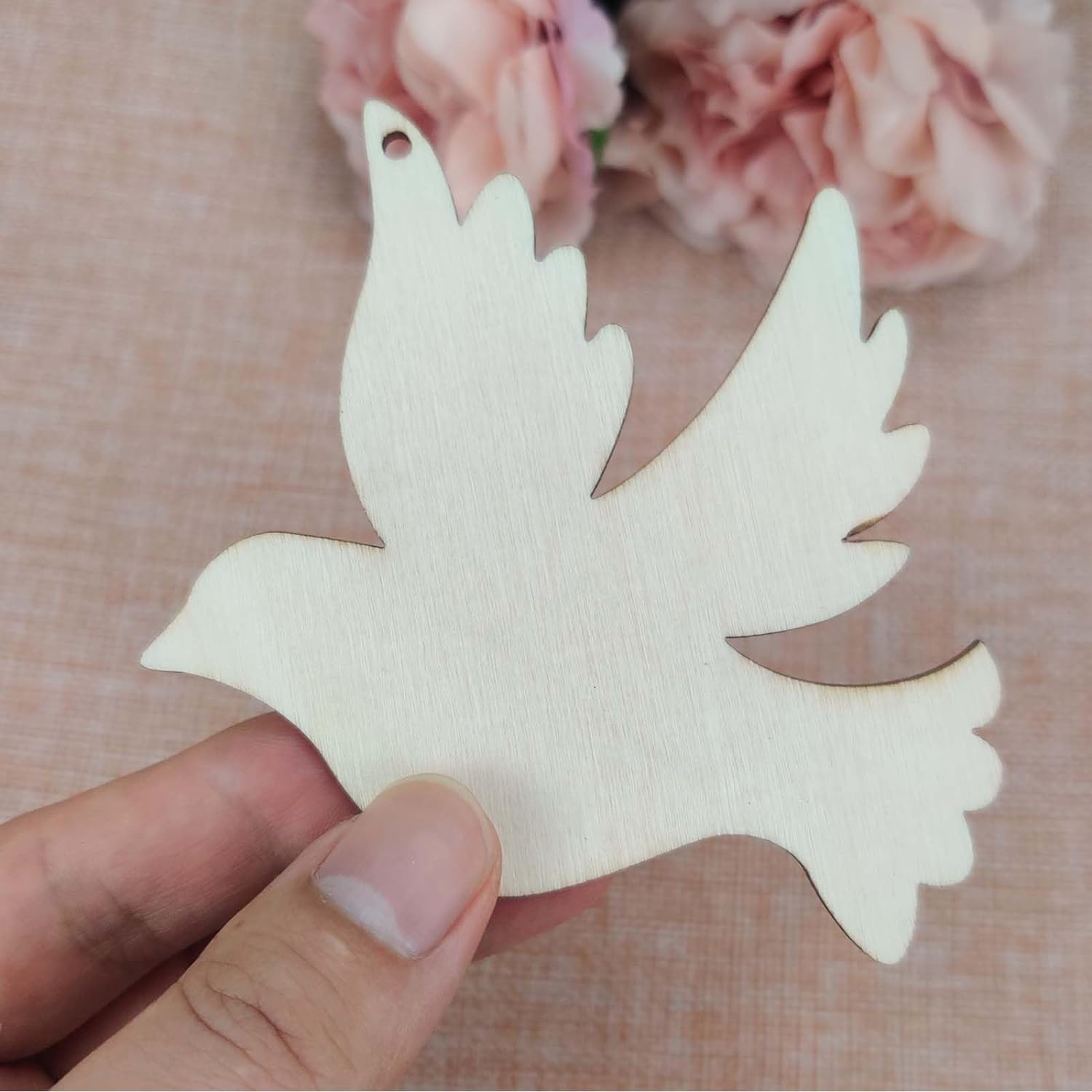 Wooden dove ornament held by a hand with a soft pink floral background