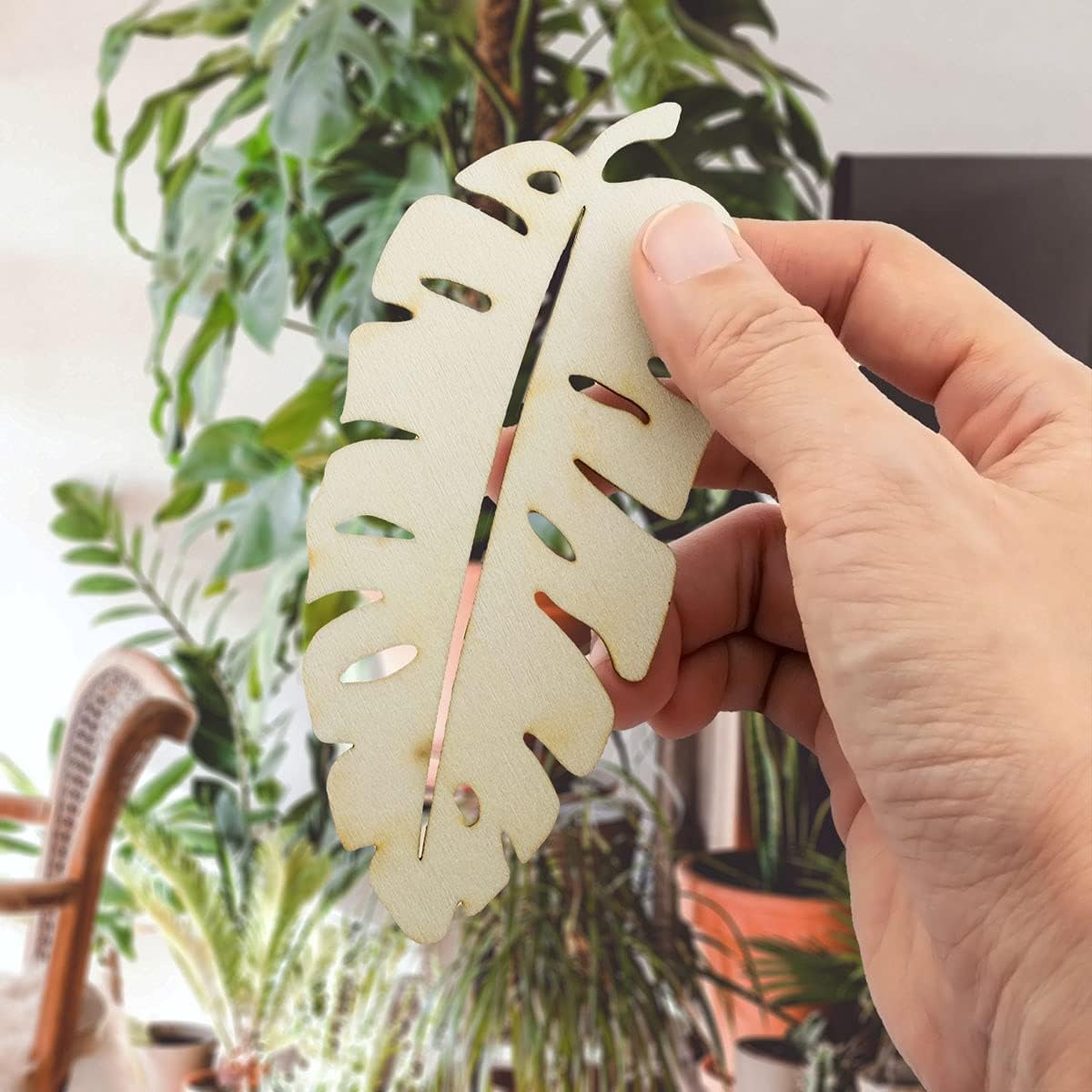 Hand holding a decorative leaf-shaped item with plants in the background