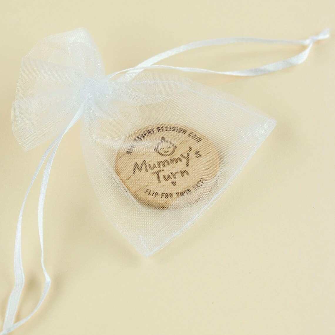 Wooden coin with 'Mummy's Turn' text in a sheer bag on a beige background