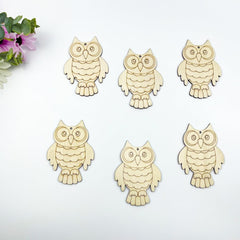 Six wooden owl ornaments on a white background with a small bouquet of flowers.