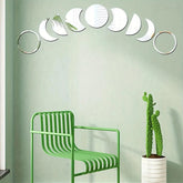 Decorative wall mirrors shaped like moons on a light green wall with a green chair and potted plant.