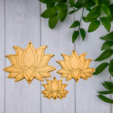 Three wooden lotus flower ornaments on a light wooden background with green leaves.