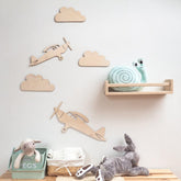 Children's room with wooden airplanes, clouds, and plush toys on a light gray wall.