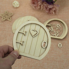 Wooden fairy door with heart design held by a hand on a textured surface with decorative elements.