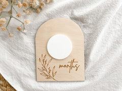 Wooden baby milestone card with 'months' and floral design on a white fabric background