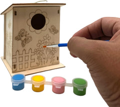 Wooden birdhouse with paint designs, hand holding a brush, and small containers of paint on a white background