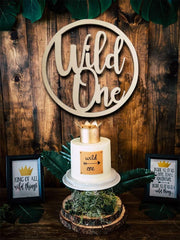 Small cake with 'Wild One' decoration on a wooden stand against a rustic wooden background.