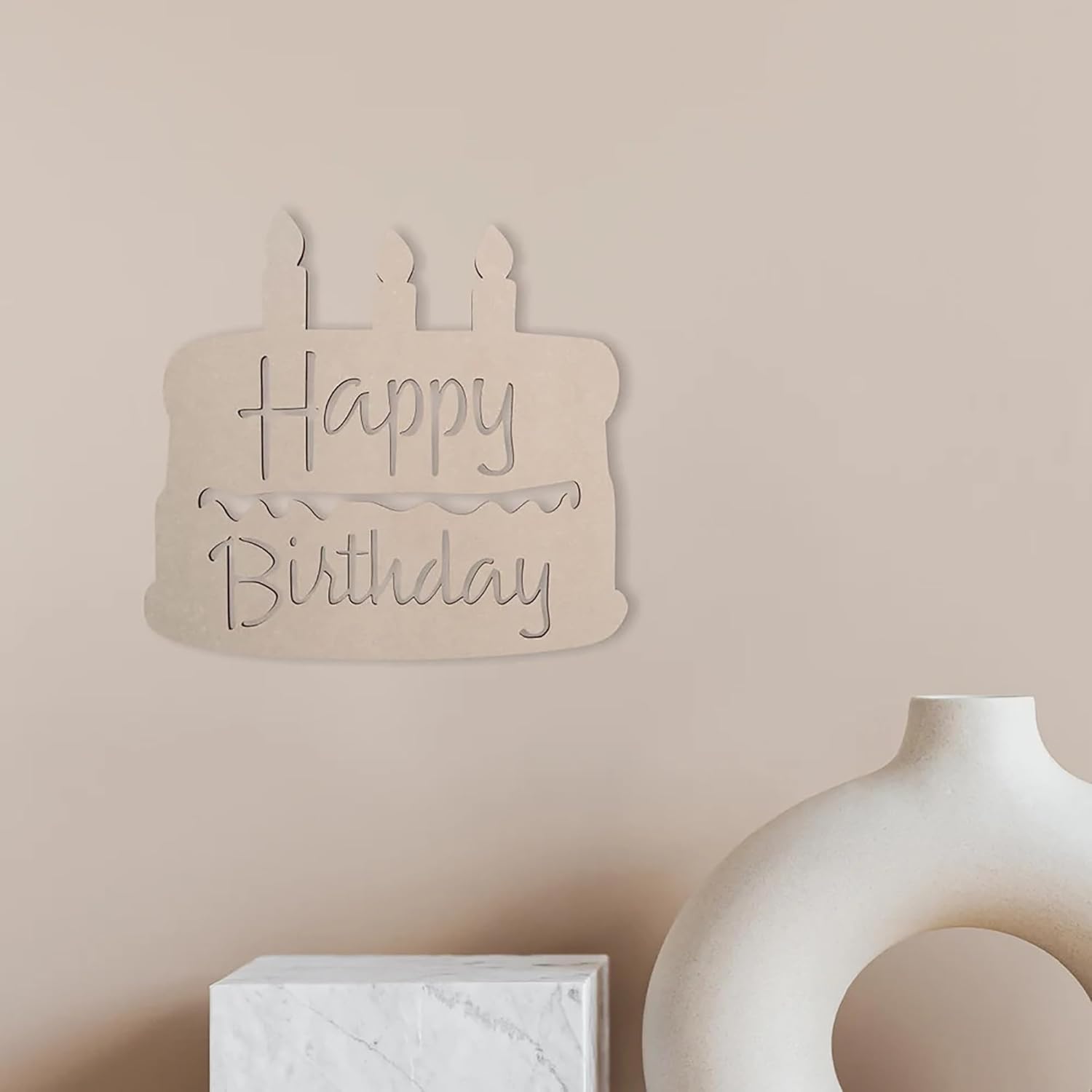 Wooden 'Happy Birthday' sign on a beige wall with a vase and box in the foreground.