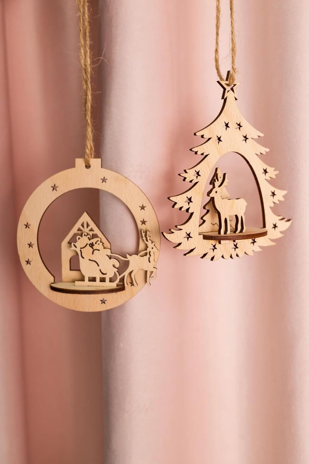 Two wooden Christmas tree ornaments on a pink background