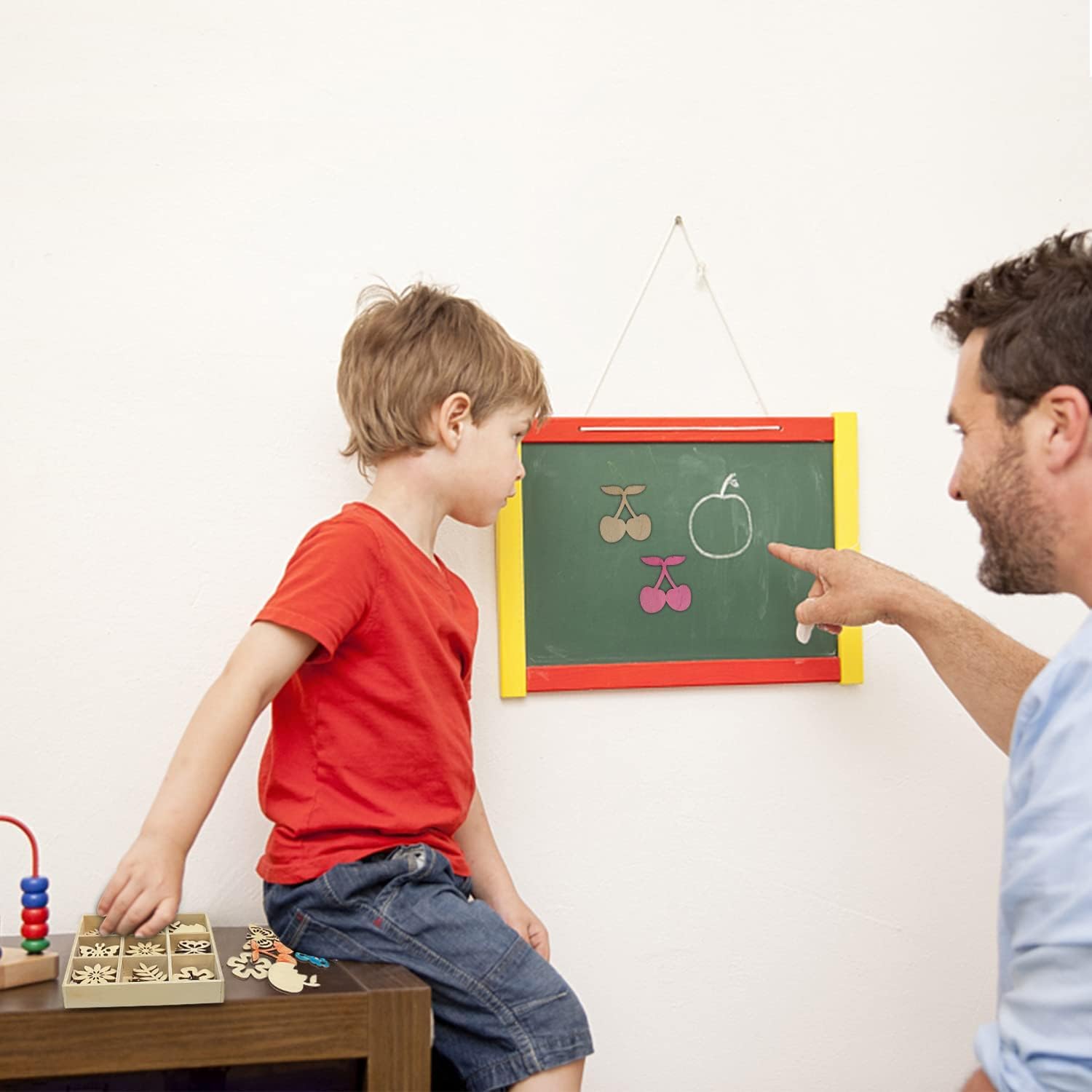 Man and child interacting with a small chalkboard on a white wall