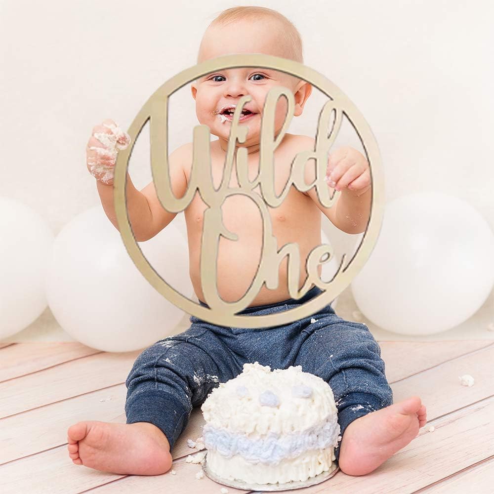 Baby sitting with a 'Wild One' sign and a small cake on a wooden floor.