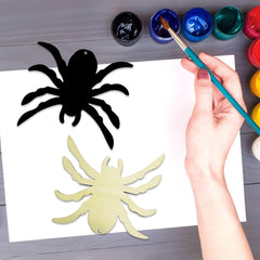 Hand painting a yellow spider on white paper with black spider template and paint supplies.